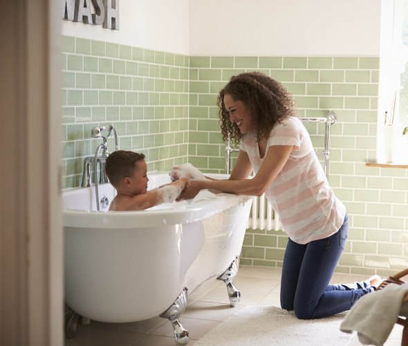 A mom bathes her son in a clawfoot bathtub.