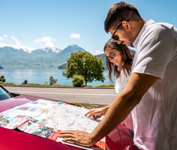 man and woman in switzerland reading map on hood of car