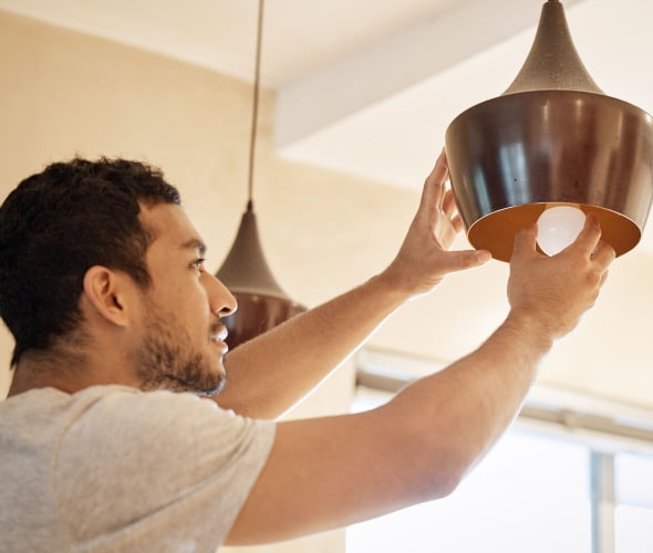 A man replaces a light bulb in a pendant light.