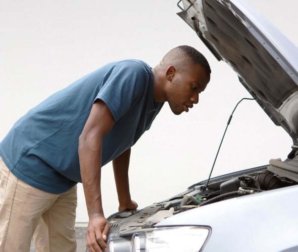 A young man looks under the hood of his car.