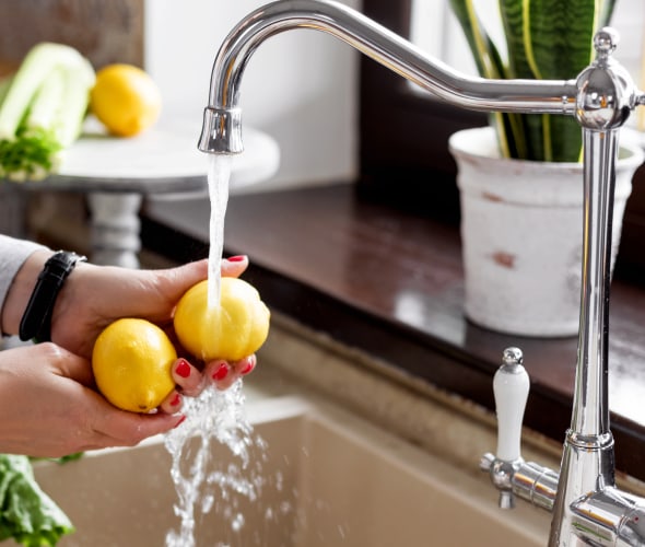A woman washes lemon at the kitchen sink.