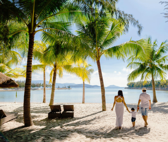 A family walks together on a white sand tropical beach.