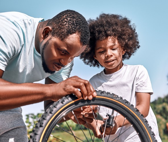 A dad and his son add air to the son's bike tire.