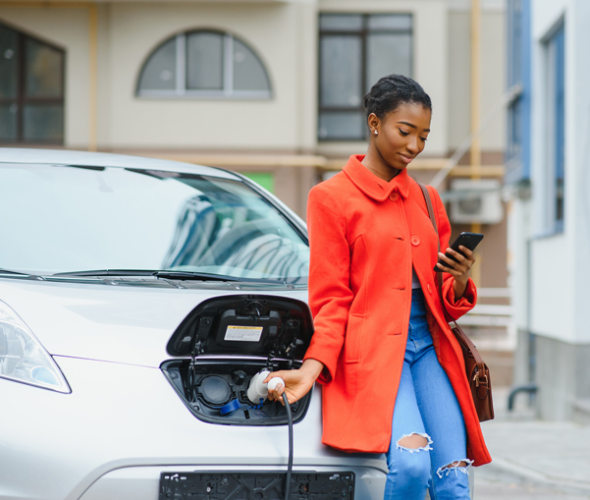 a woman stands by her EV holding the car charger while it's charging