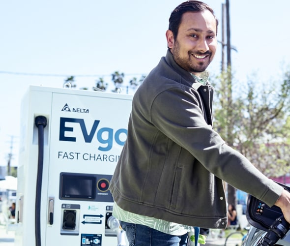 a man smiles while he charges his electric car at an EVgo fast charging station