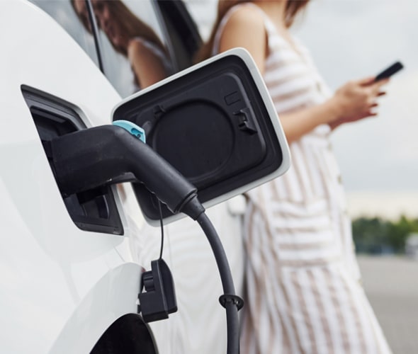 A women on her phone stands by her white electric car while it charges
