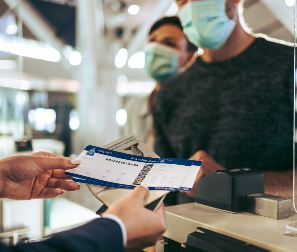 Two travelers pick up their boarding passes from the airport check-in counter.