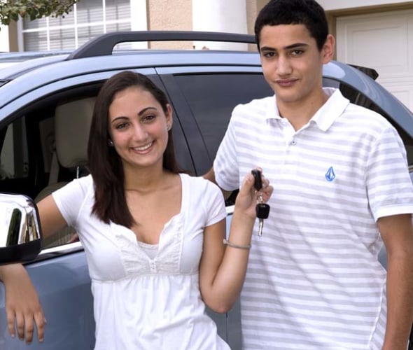 two teenagers in front of a car, the female holds up car keys after successful completion of the driver education course