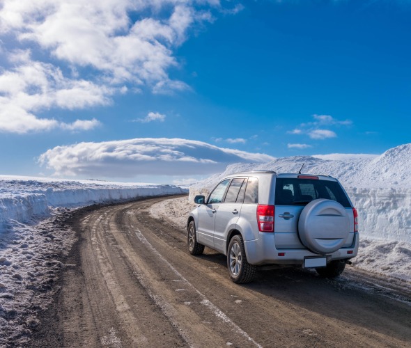 A small SUV drives on a plowed road in Iceland.