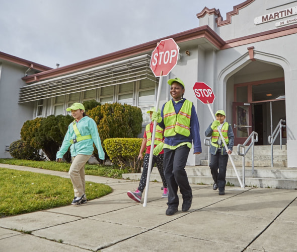 Students who participate in the AAA School Safety Program walk outside of their school with safety vests and stop signs.