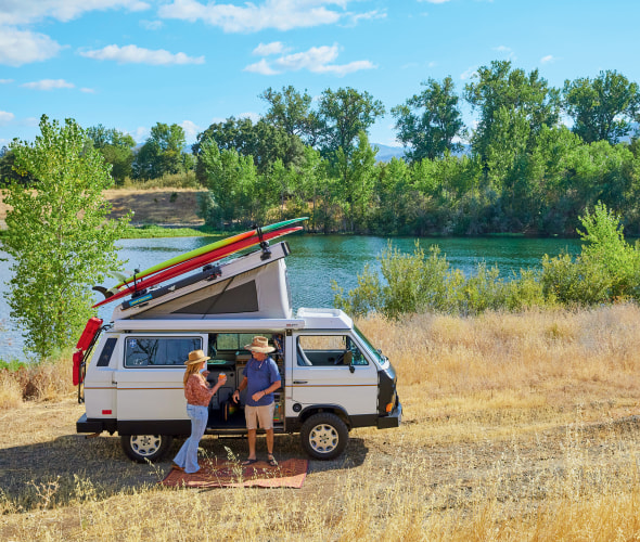 Nanci and Skip Williams outside of their 1987 Volkswagen Vanagon Westfalia along a river in California.