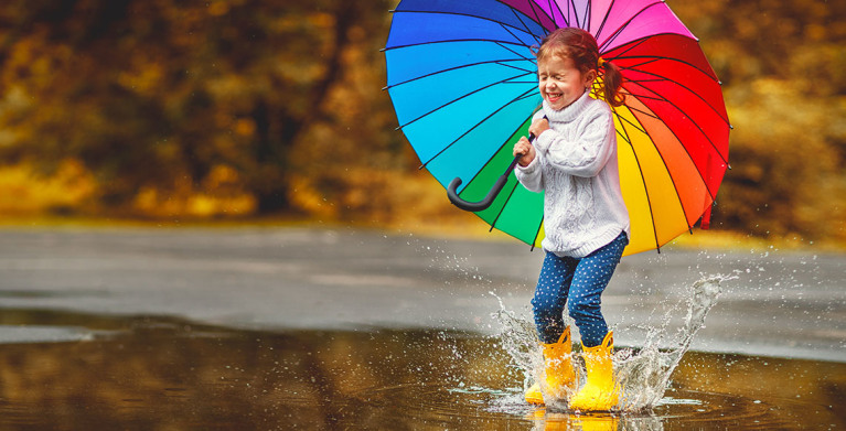 a young girl splashing in the rain with a rainbow umbrella