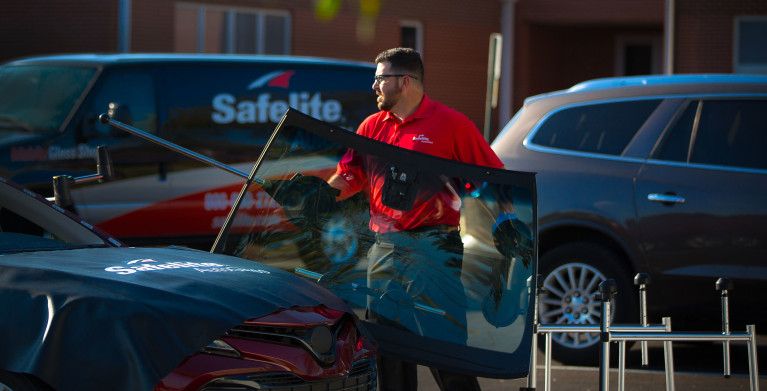 Safelite autoglass technician replacing a windshield with his van parked in the background