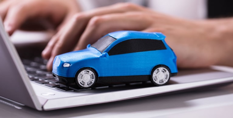 a blue toy car sits on a laptop while someone types