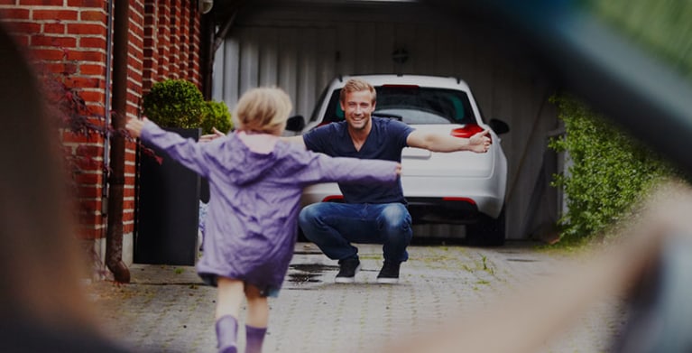 Father greets his daughter in his driveway in front of his car protected by AAA Insurance.