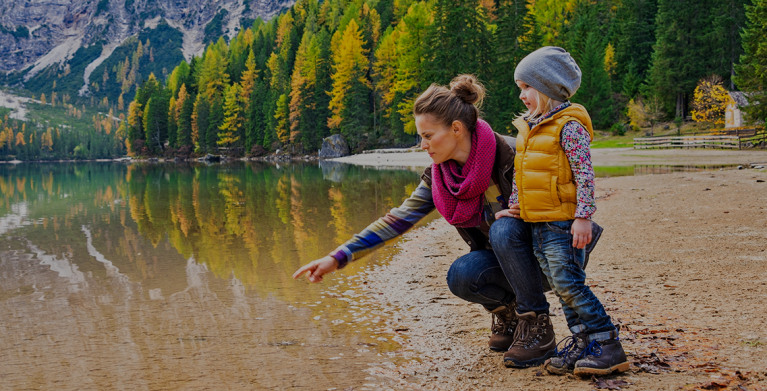 mother with aaa classic membership kneels next to child at a mountain lake