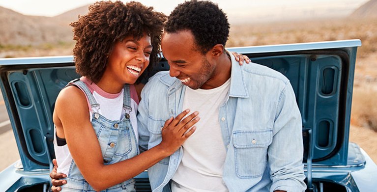 a couple sits on the back of their car while waiting for AAA roadside service