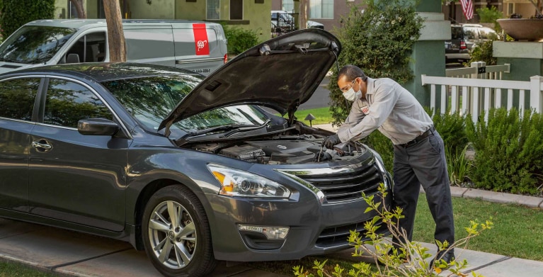 AAA auto repair mechanic checking a car in a driveway.