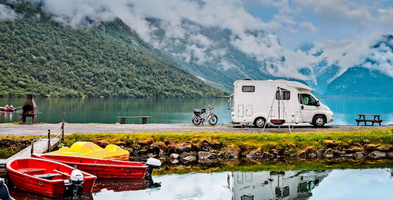 rv and motorcycle protected by AAA insurance parked at a lake in the mountains with boats in it