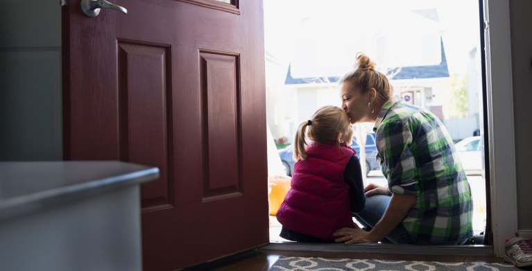mother kissing her daughter on the head in the doorway of her home protected by AAA insurance.