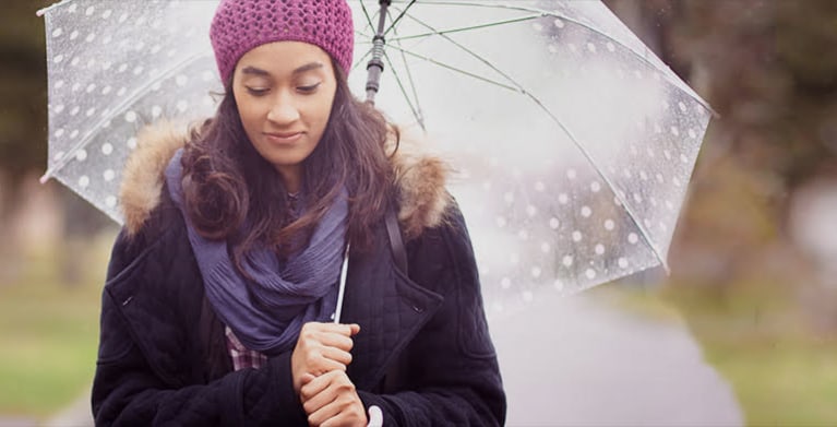 a woman with AAA insurance stands under an umbrella in the rain