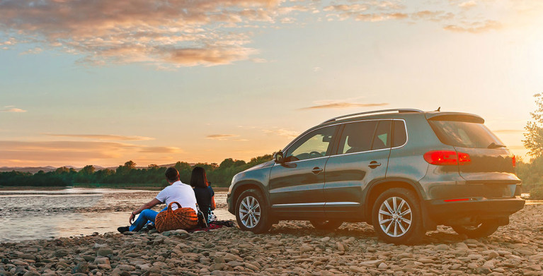 AAA members picnic next to their car on a rocky beach at sunset