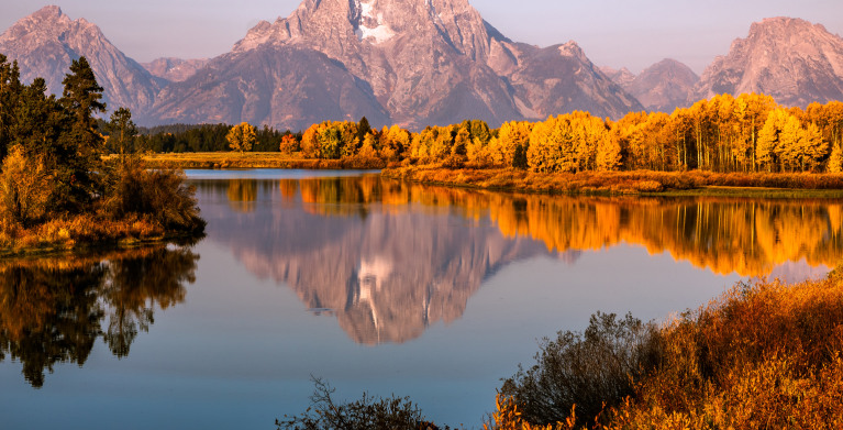 Trees with autumn leaves reflect in the Snake River in Grand Teton National Park.