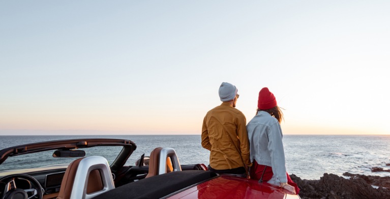 Man and woman sitting on car and watching sunset