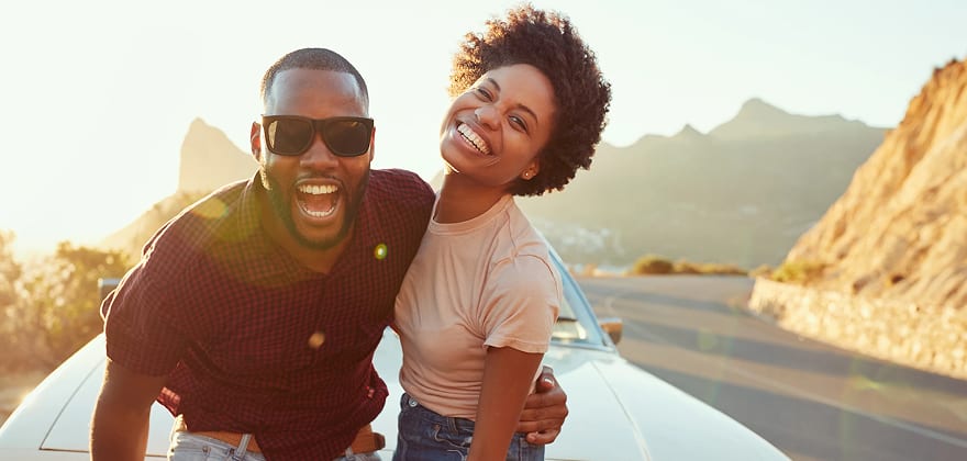 a couple smiles in front of their car