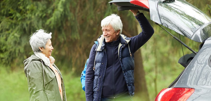 two older drivers stand behind an open car trunk getting ready to go for a walk