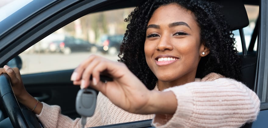 teen in their new car holding the key out the window and smiling