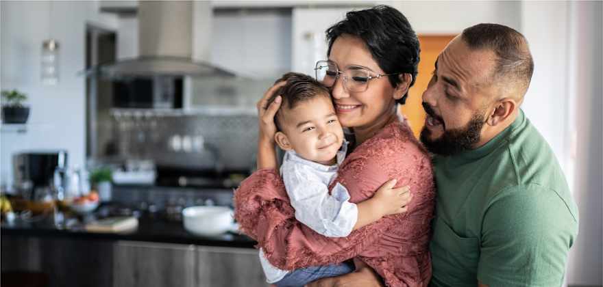 a family with a baby stands in the kitchen smiling, thanks to the feeling of security with a certificate of deposit