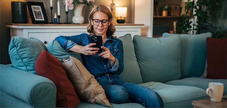 person sits on a couch while reviewing their high-yield savings account on their mobile phone