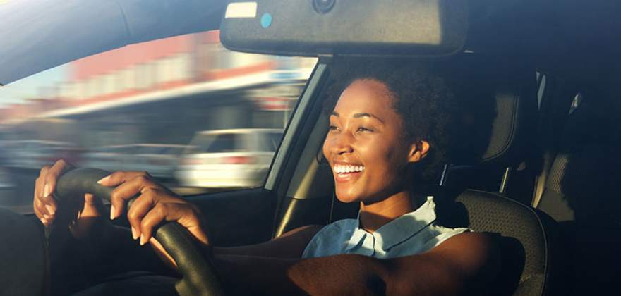 a smiling AAA member with AAA auto insurance drives her car