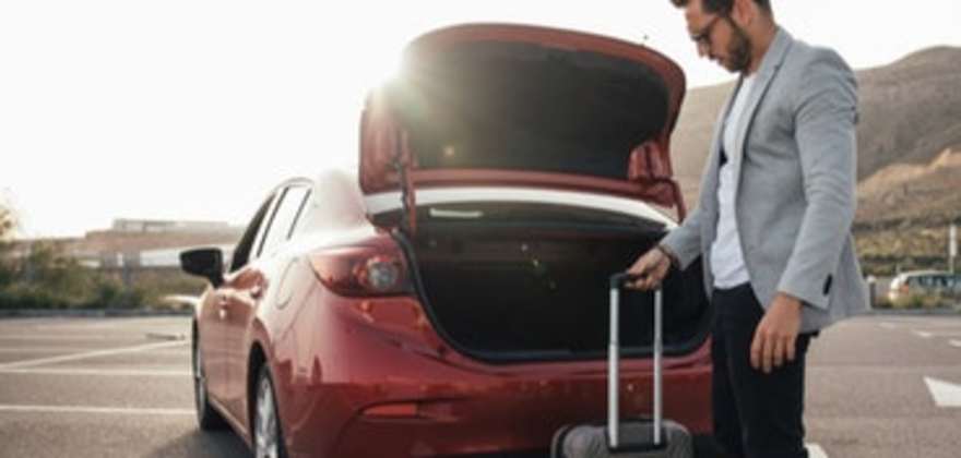 man puts suitcase into his rental car booked through AAA Travel