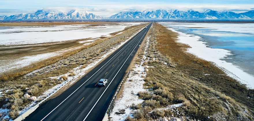 Cars drive on a road surrounded by a dusting of snow.