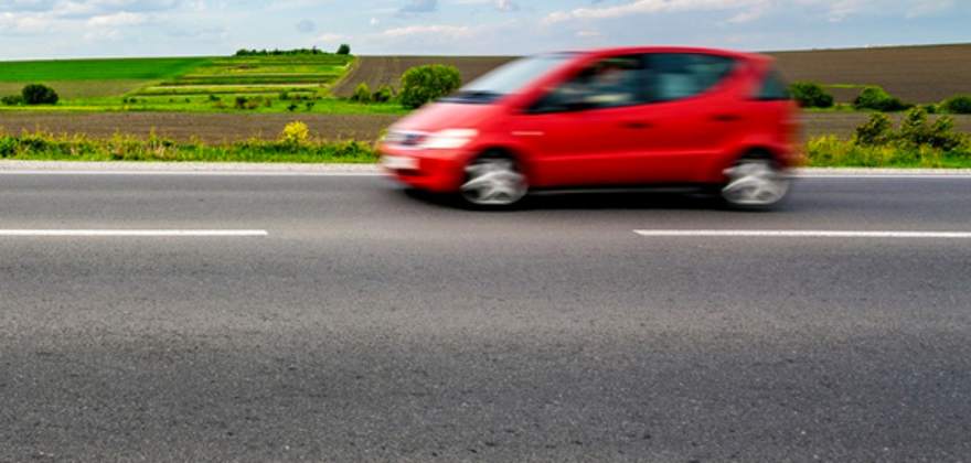 A blurred red car drives along the road