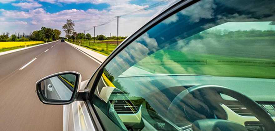Car driving fast on two lane street with clouds reflecting in window