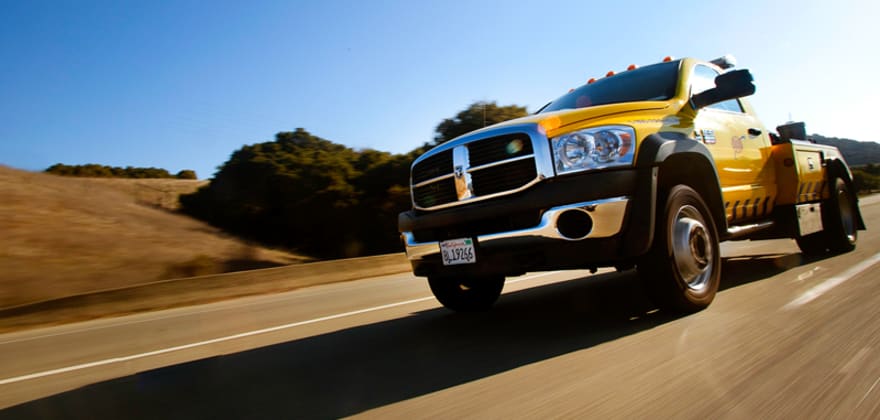 AAA tow truck on the road with blue skies and hilly roadside