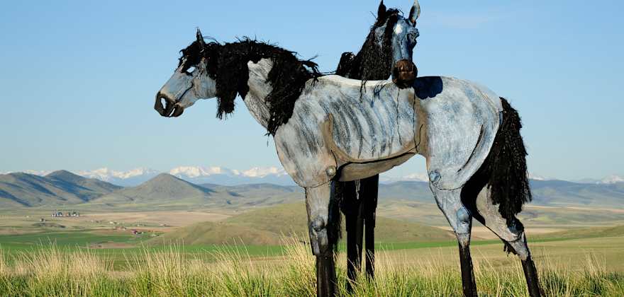 Two of the large metal Bleu Horse sculptures standing in a grassy prairie near Three Forks, Montana