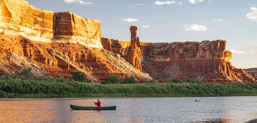 A person paddles up the green river at sunset.