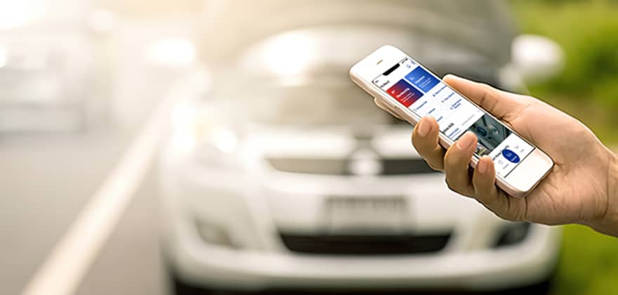 Hand of a AAA Member using the AAA app on their cellphone to call for roadside assistance, with broken down car in the background.