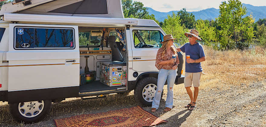 Nanci and Skip Williams outside of their 1987 Volkswagen Vanagon Westfalia along a river in California.