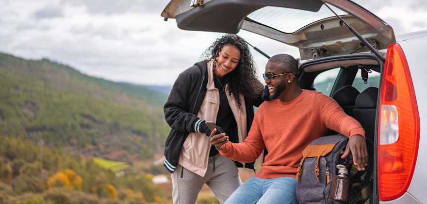 AAA Members look at their phone by their car at a scenic vista