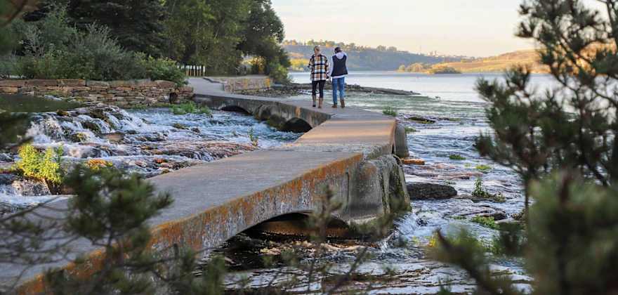 people walk along a scenic pathway near trees and water in Great Falls, Montana