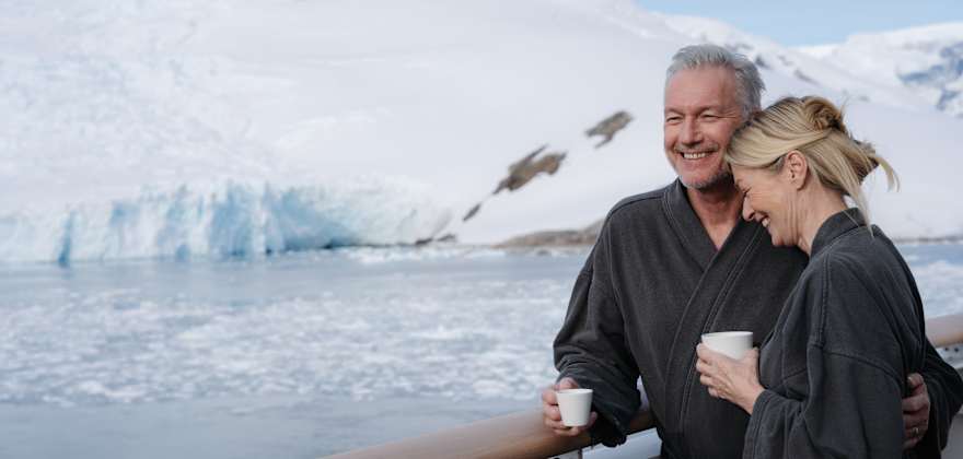 couple having coffee on ship balcony overlooking icebergs