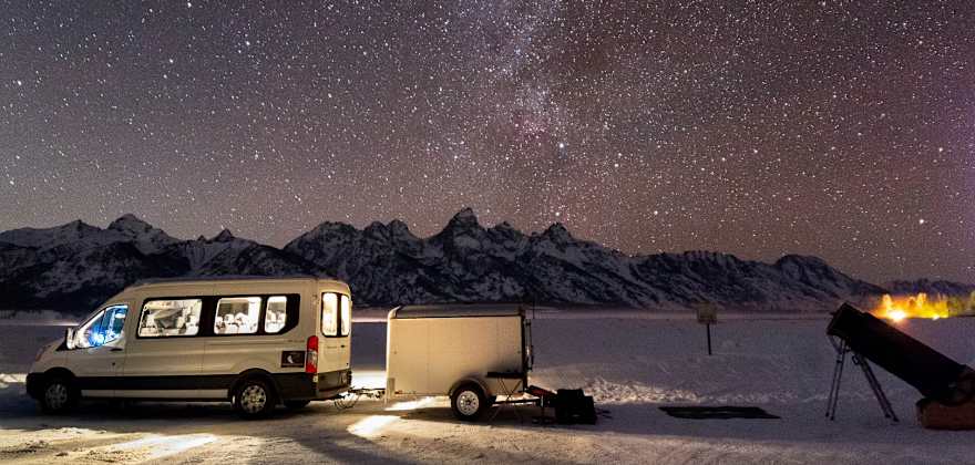 a van is parked near a telescope with a brilliant starry sky and mountains in the distance
