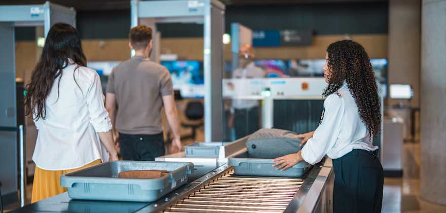 A TSA employee feeds bags through an x-ray machine as travelers go through metal detectors in the airport.