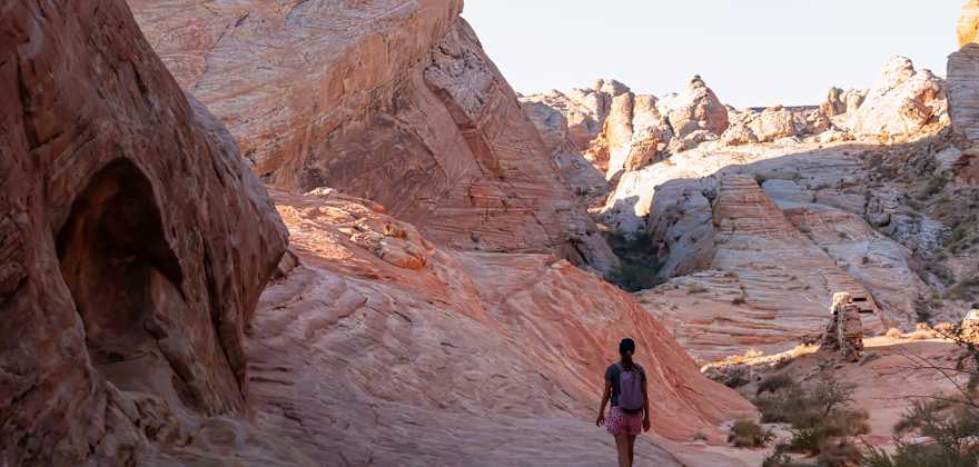 Woman with scenic sunrise view of arid landscape with striated red and white rock formations along the White Domes Hiking Trail in Valley of Fire State Park in Mojave desert, Overton, Nevada,