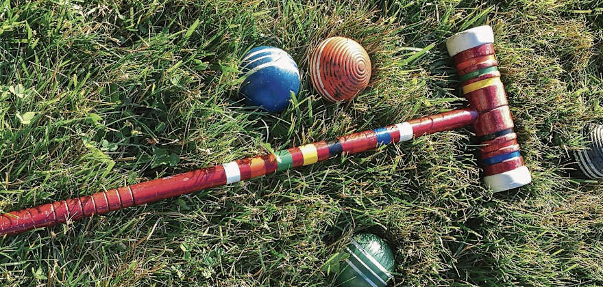 a red croquet mallet with a colorful croquet balls lying on grass